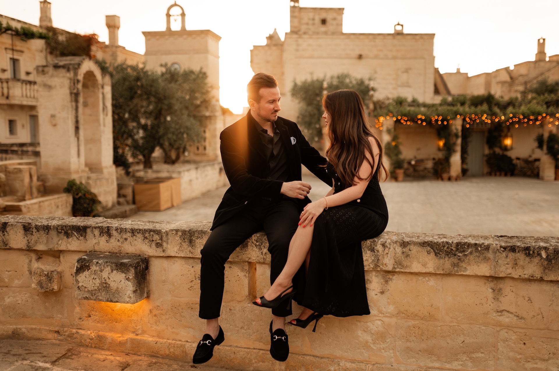 Heather and Josef at golden hour, seated on a stone wall in a sunlit Italian courtyard